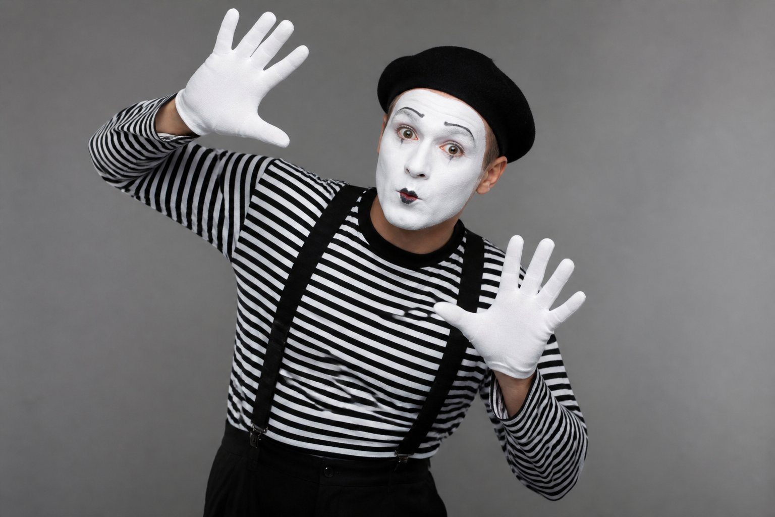 Artista mímico com rosto pintado de branco, usando roupa preta e branca, fazendo um gesto clássico de mímica contra fundo neutro.